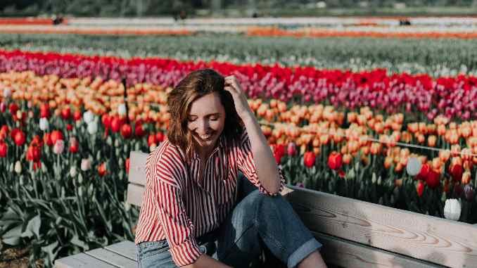Frau sitzt lächeln auf einer Bank umgeben von einem Blumenmeer