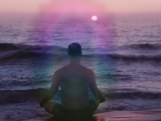 Mann mit violetter Aura der meditierend am Meer sitzt