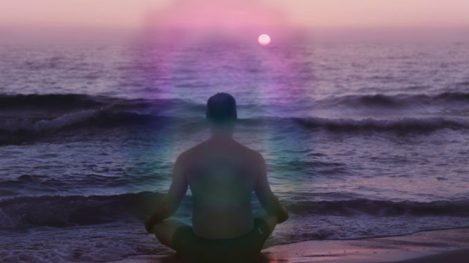 Mann mit violetter Aura der meditierend am Meer sitzt
