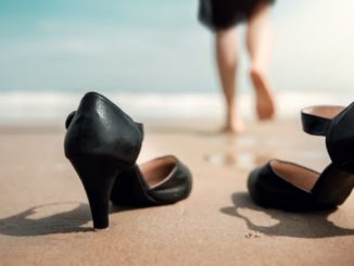 Frau die ihre Schuhe stehenlässt und barfuss ins Meer geht