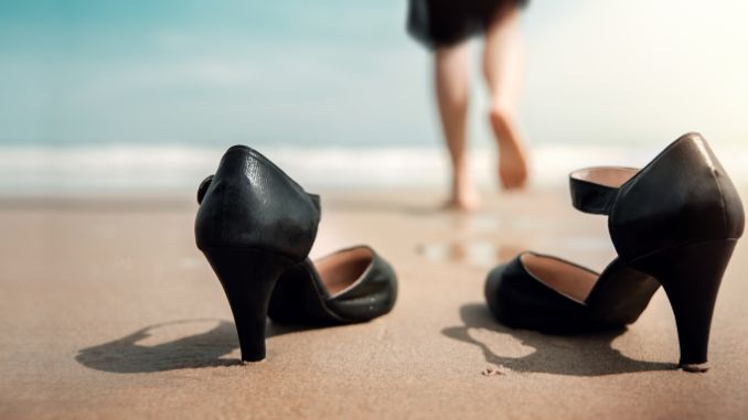Frau die ihre Schuhe stehenlässt und barfuss ins Meer geht