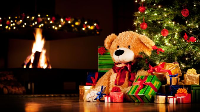 Teddy mit Weihnachtsgeschenken vor Tannenbaum