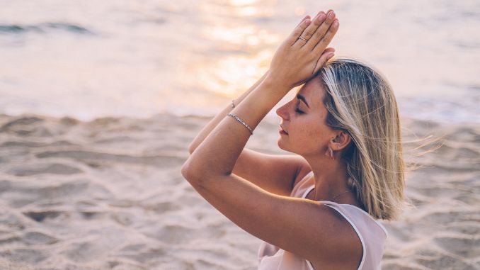 Frau sitzt am Strand und macht yoga