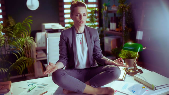 Frau sitzt auf ihrem Schreibtisch und meditiert
