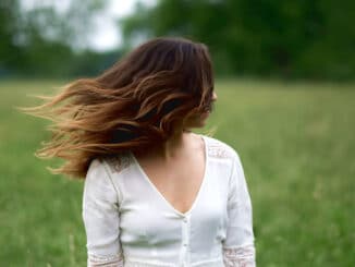 Frau steht mit wehenden Haaren auf einer Wiese