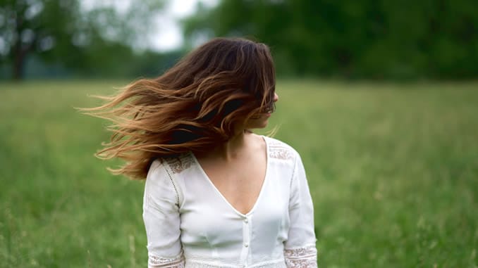 Frau steht mit wehenden Haaren auf einer Wiese