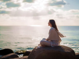 eine Frau sitzt auf einem Felsen am Meer