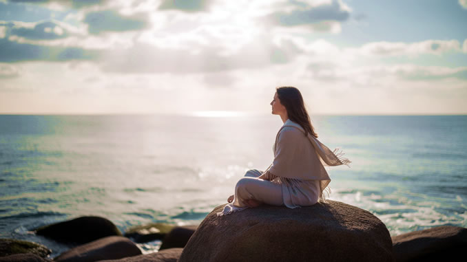 eine Frau sitzt auf einem Felsen am Meer